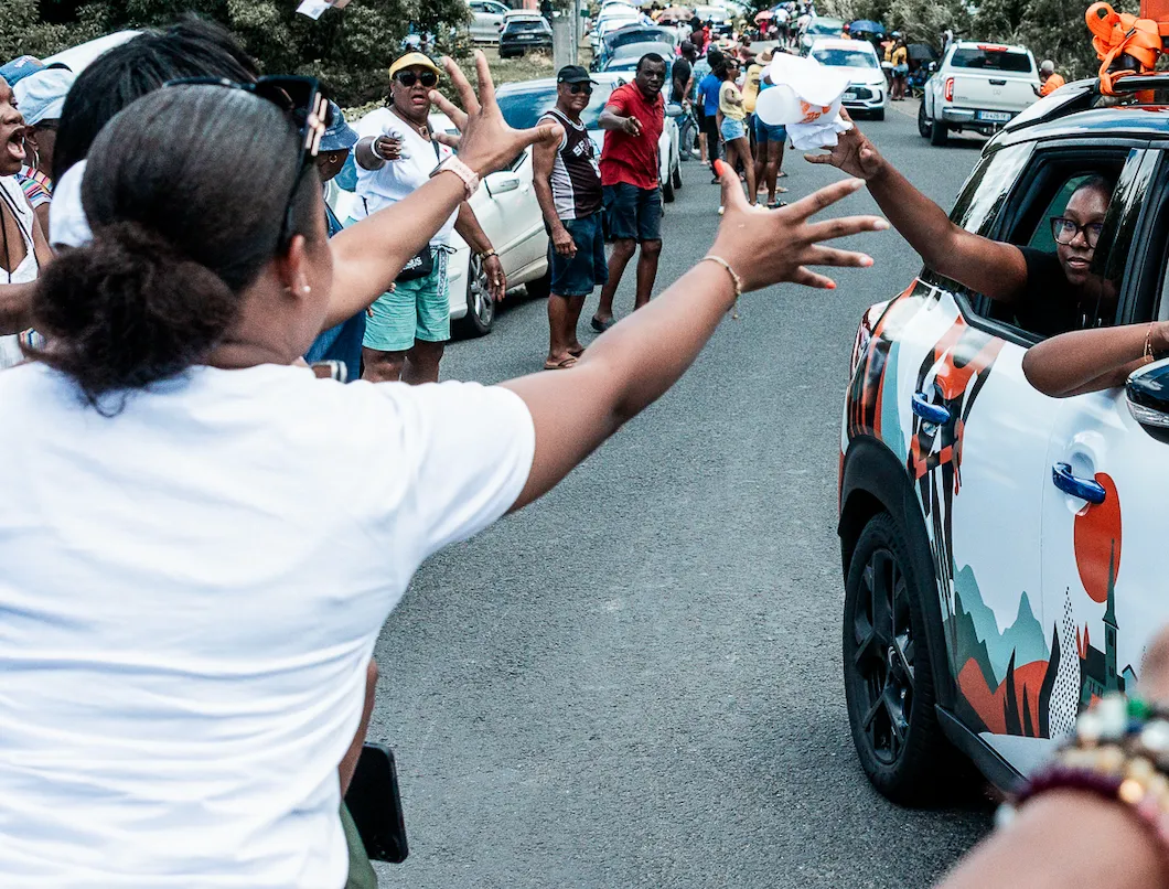 Distribution de goodies depuis un véhicule de la caravane publicitaire du Tour cycliste de la Guadeloupe, bras tendus des spectateurs au bord de la route